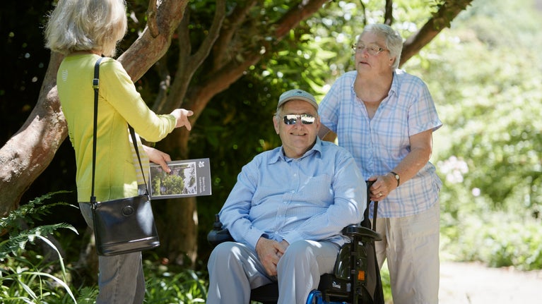 Man sat in wheelchair with two ladies standing in garden setting